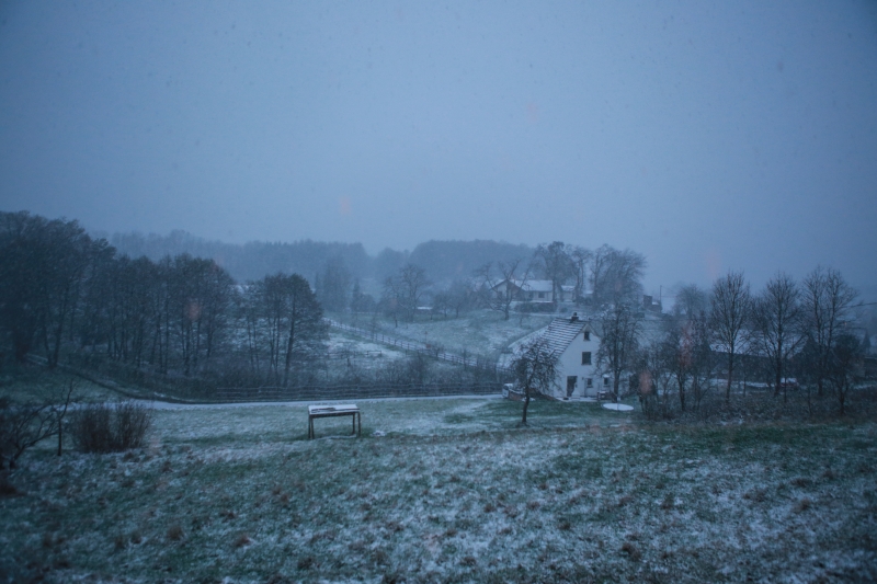Verschneite Hügellandschaft mit Häusern und Wald