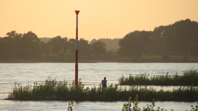 Angler mit Rute an einem Fluss im Abendlicht