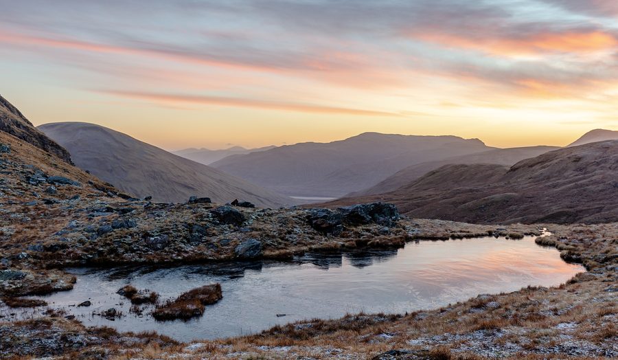 Kleiner See zwischen Bergen in den schottischen Highlands bei Sonnenaufgang