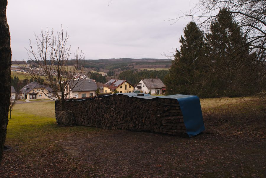 Blick auf Neuhütten von einem Weg zum Dollberg mit Holzstapel im Vordergrund