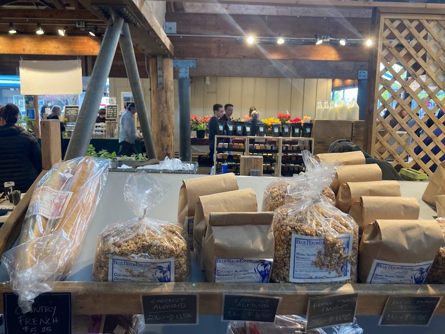 Display of granola bags at Olympia Farmers Market, with flowers and people in the background
