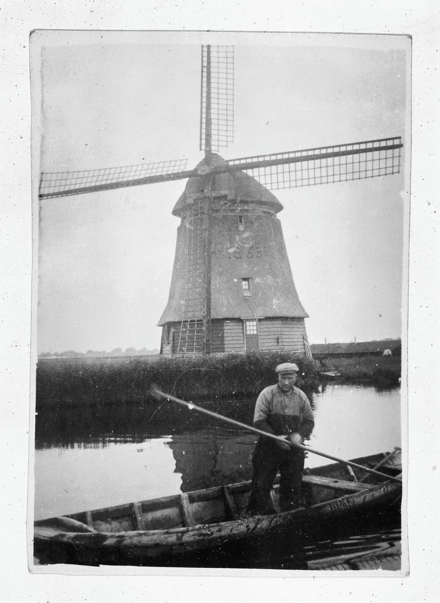 Een man in een roeiboot voor Molen D van de polder Geestmerambacht bij Broek op Langedijk