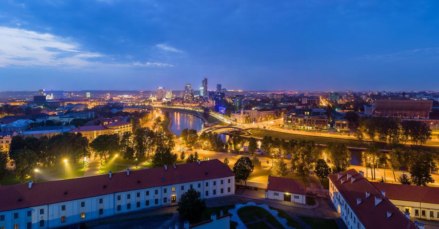 Skyline von Vilnius bei Dämmerung mit beleuchteten Gebäuden.