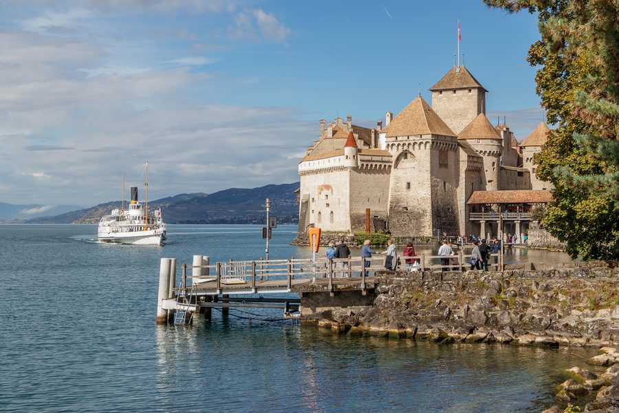 Schloss Chillon am Ufer des Genfersees, während sich ein historisches Dampfschiff nähert.