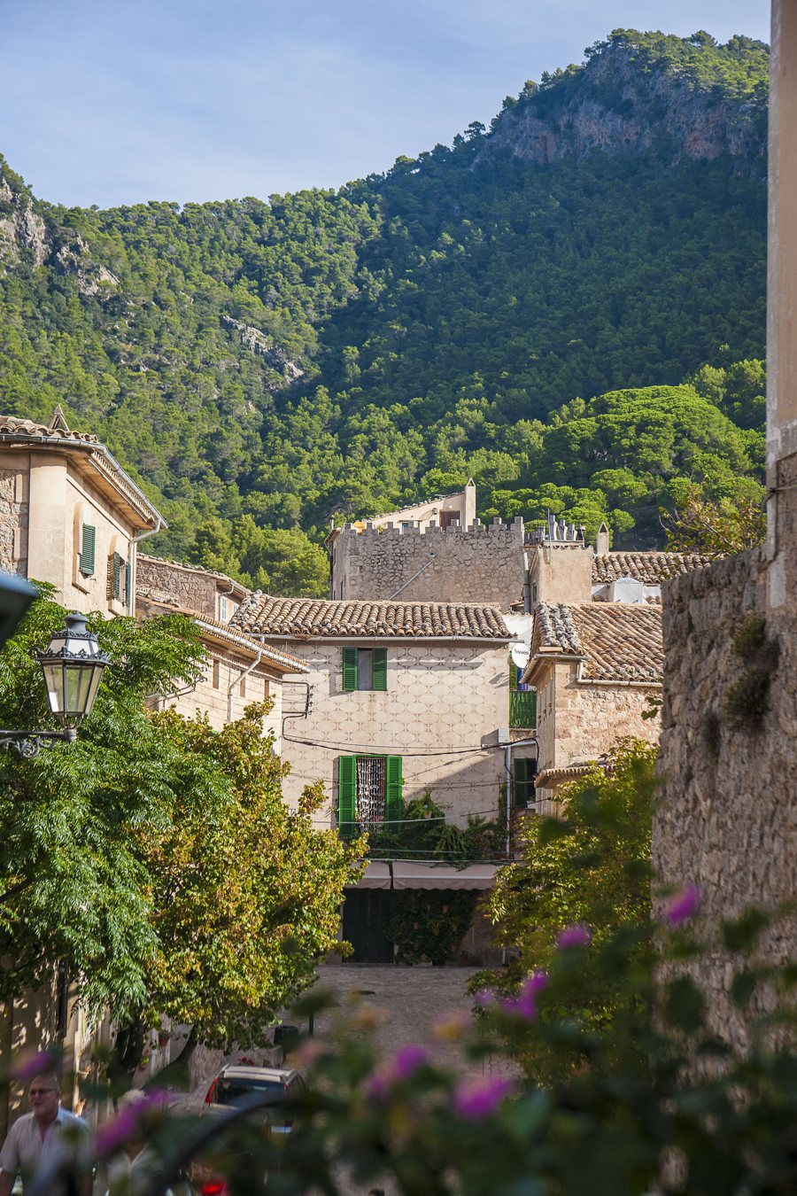 Dorfstraße mit Steinhäusern und grünen Fensterläden vor bewaldeten Bergen in Spanien