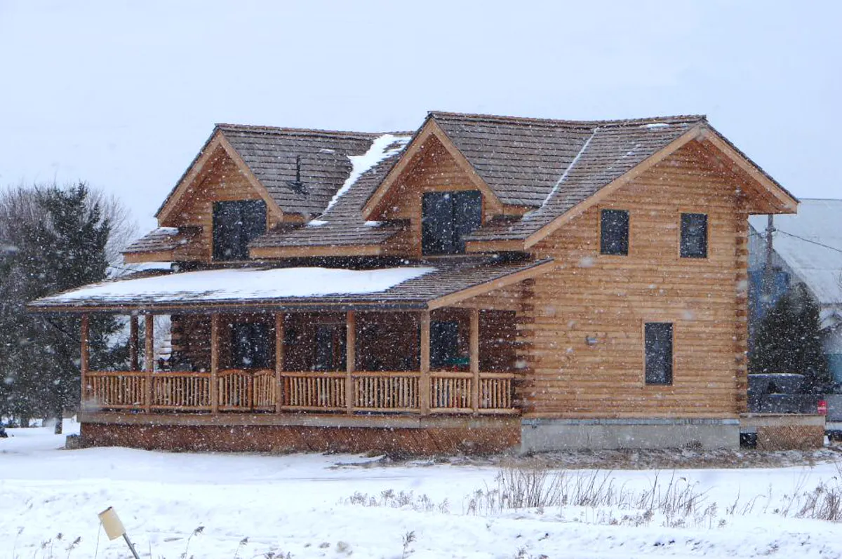 Modernes Holzferienhaus im Schnee mit überdachter Holzterrasse
